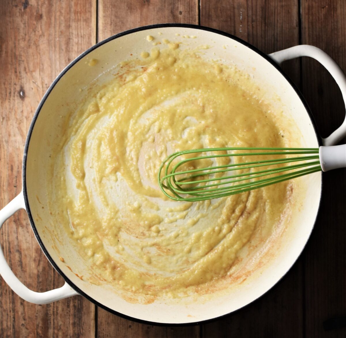 Top down view of roux in large shallow white pan with green whisk.