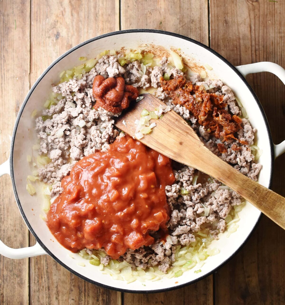 Ground turkey, tomatoes and tomato paste in large shallow white dish with wooden spoon.