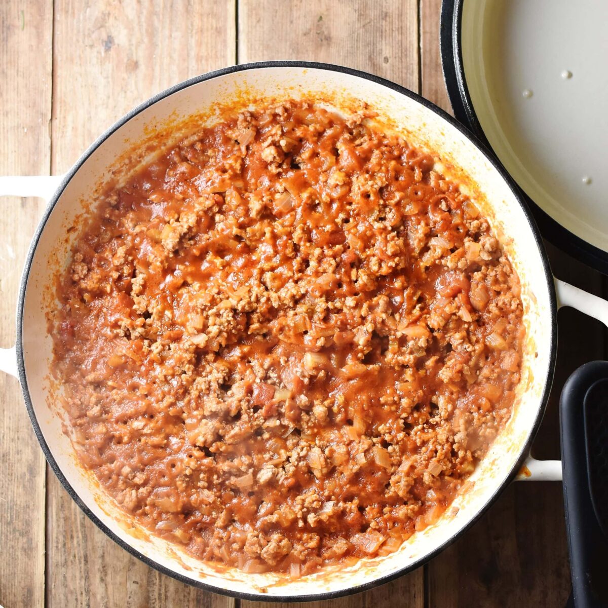 Thick tomato meat sauce in large shallow white pan, with white lid in top right corner.