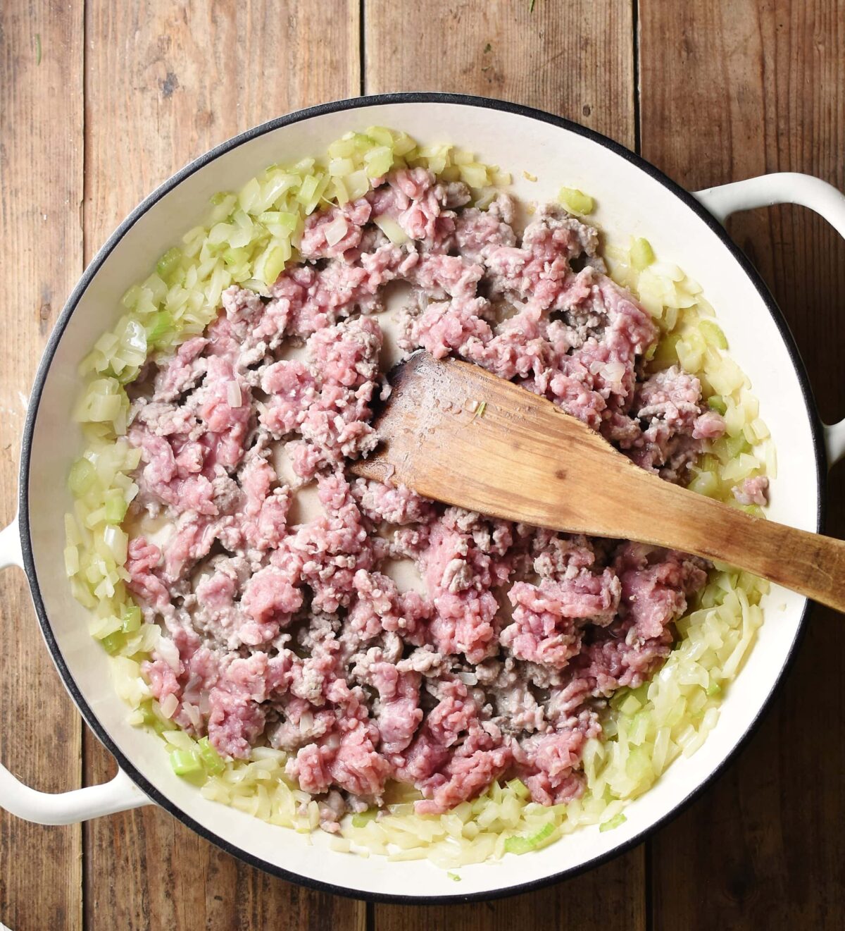 Turkey mince and chopped onions in large shallow white dish with wooden spatula.