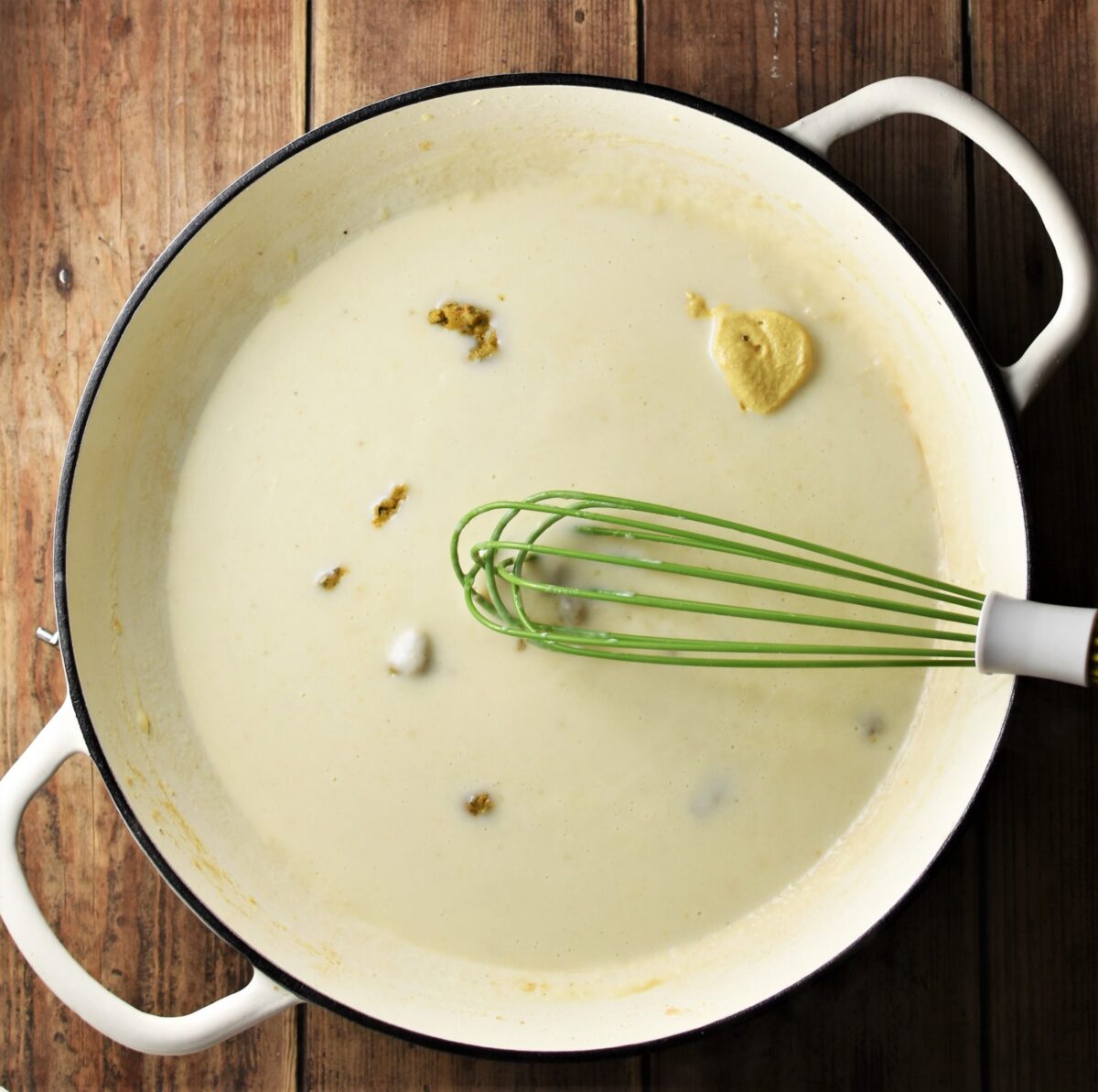 Milk, crumbled stock cube and mustard in large shallow white pan with green whisk.