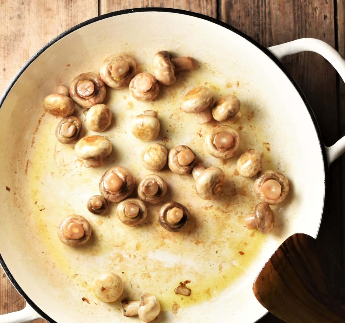 Mushrooms in large white pan with spatula in bottom right corner.