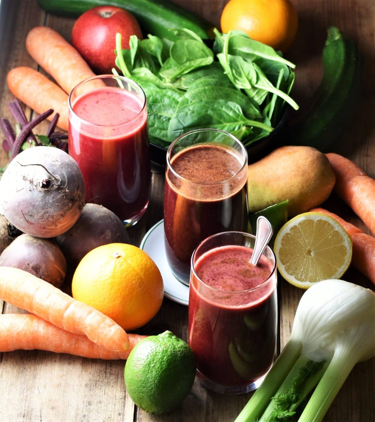 Beetroot juice in 3 glasses, with fresh fruit and vegetables in background.
