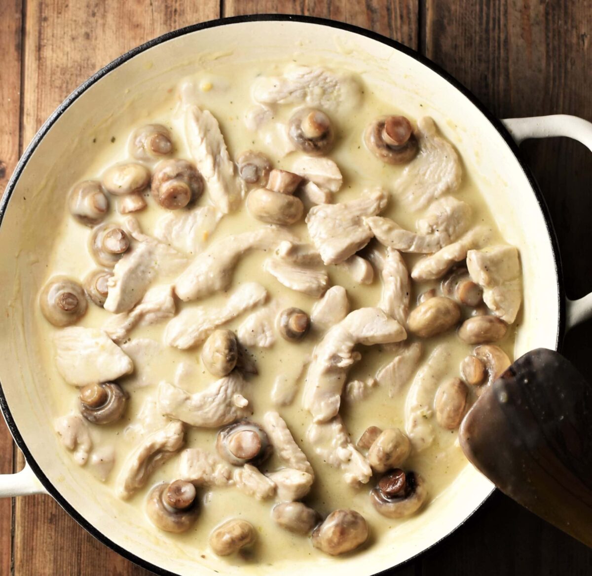 Strips of turkey and mushrooms in creamy sauce in large white pan with spatula in bottom right corner.
