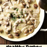 Creamy turkey stroganoff with mushrooms in large white pan with spatula to the right and chopped herbs in background.
