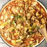Top down view of cabbage roll skillet with fresh dill and wooden spoon.
