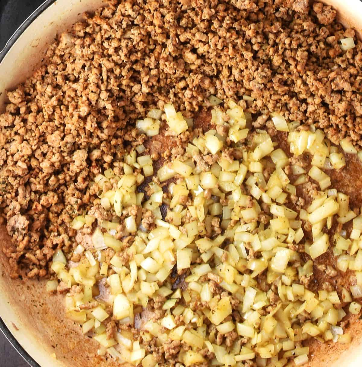 Ground meat with fried onion in large skillet pan.