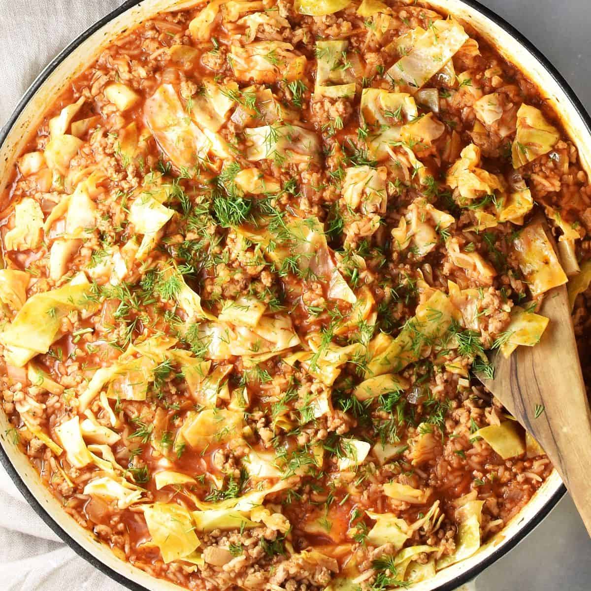 Top down view of cabbage roll skillet with fresh dill and wooden spoon.