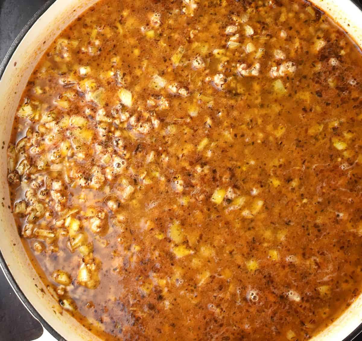 Top down view of meat and rice with stock in white skillet pan.