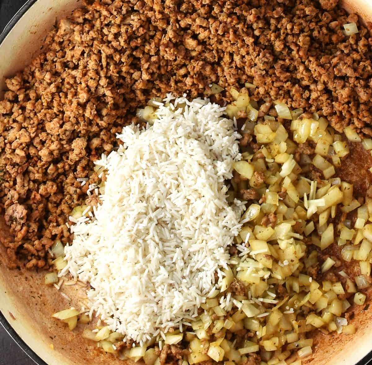 Top down view of browned ground meat, rice and onion in white skillet.