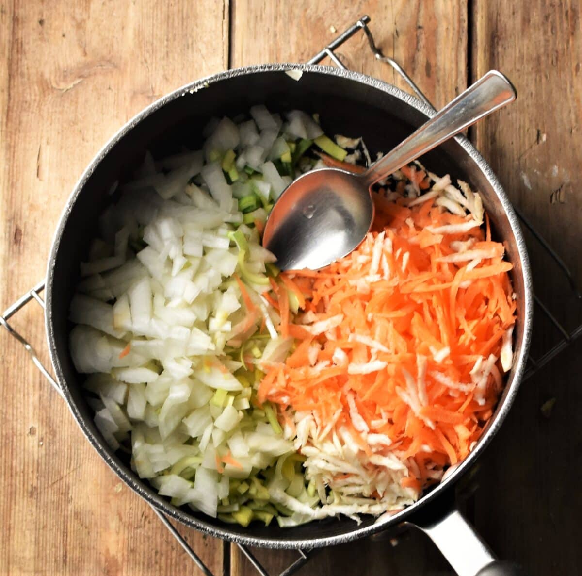 Chopped onion and grated vegetables in large pot with spoon.