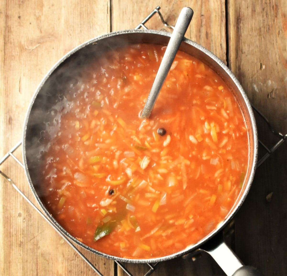 Steaming tomato and rice soup with vegetables in large pot with spoon.