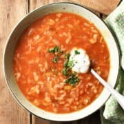 Top down view of Polish tomato rice soup with sour cream in green bowl with spoon.