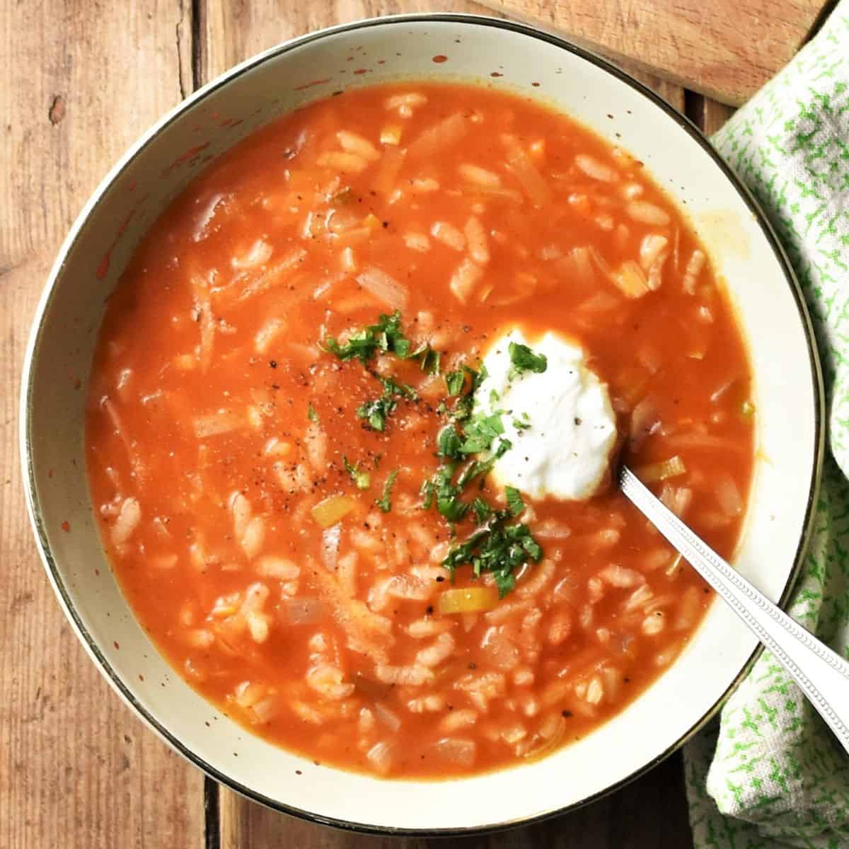 Top down view of Polish tomato rice soup with sour cream in green bowl with spoon.