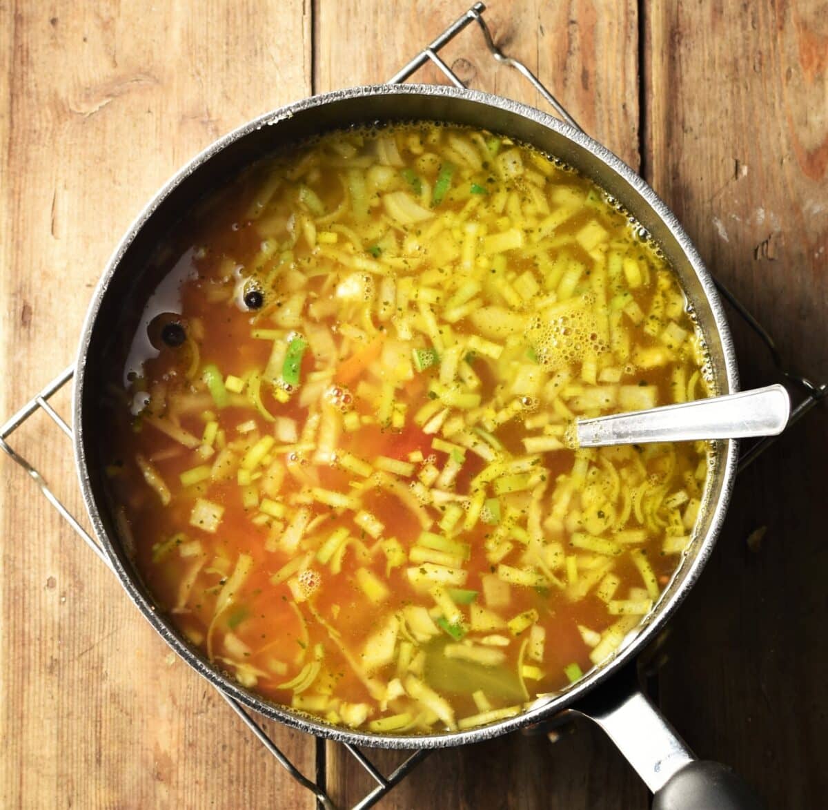 Chopped vegetables in tomato soup in large pot with spoon.