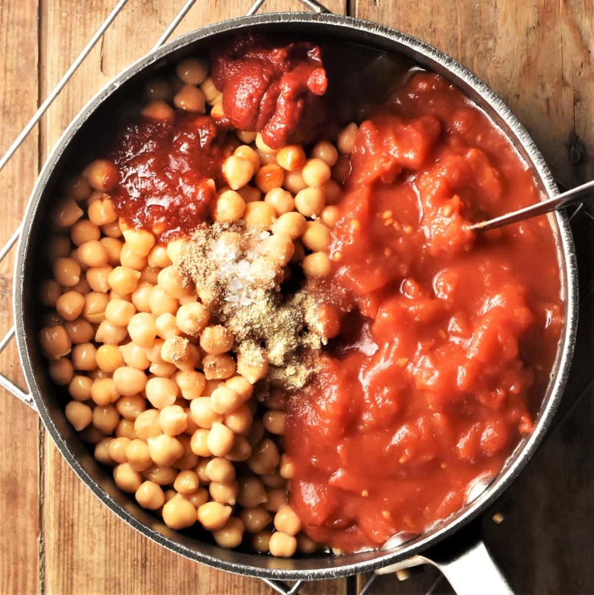 Tomato sauce and chickpeas with spices in pot with spoon.