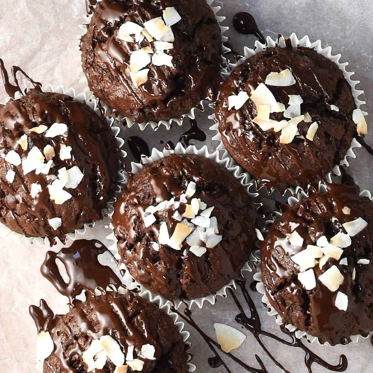 Top down view of chocolate coconut muffins with chocolate drizzle and coconut flakes.