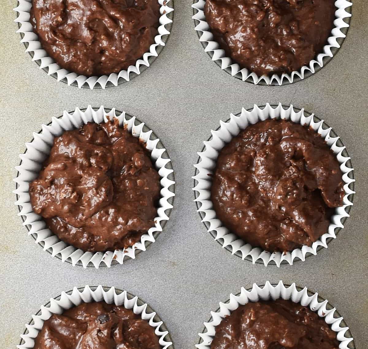 Top down view of coconut chocolate muffin batter in white cases in muffin pan.