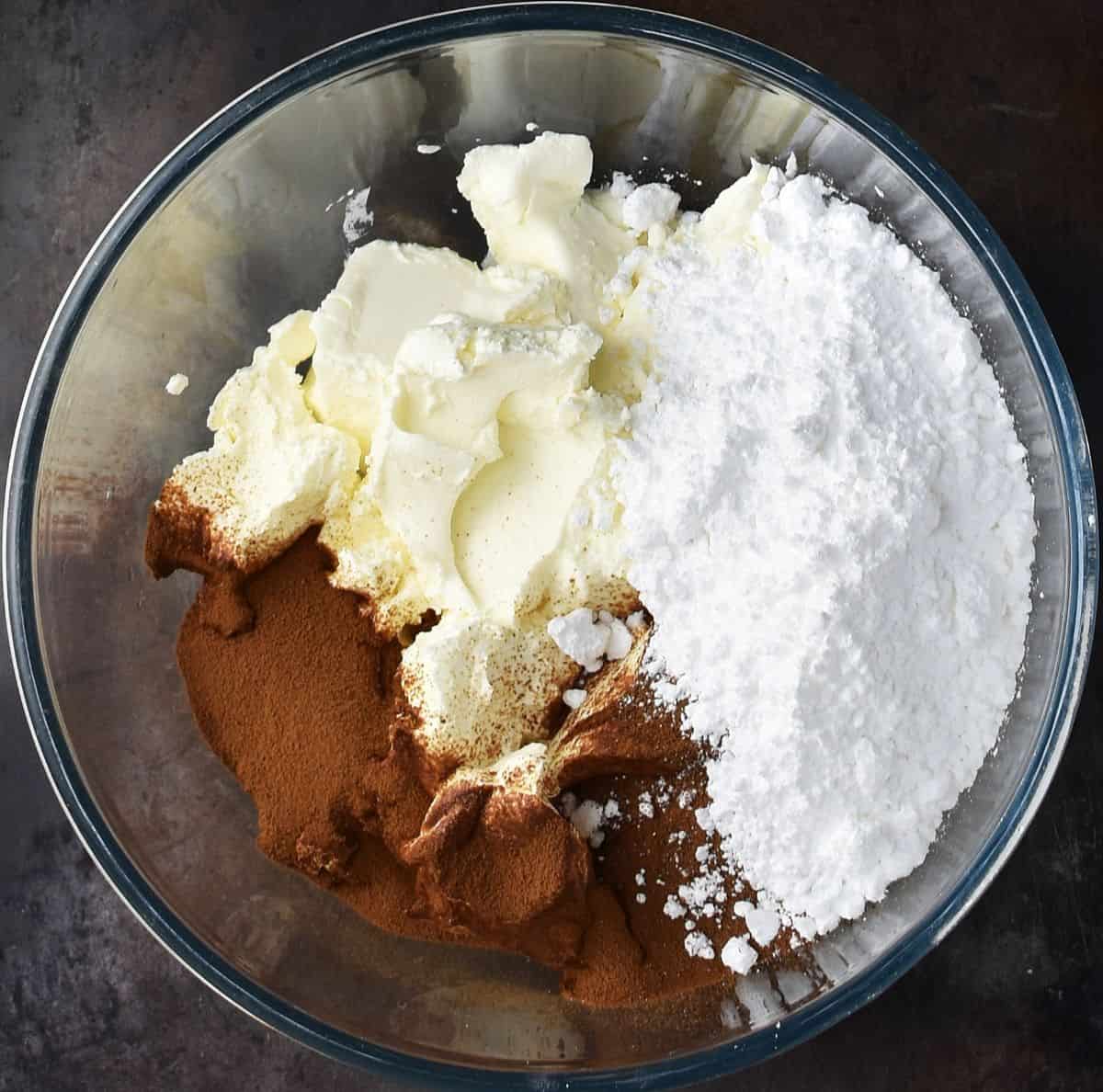Cream cheese, confectioners sugar and coffee powder in glass bowl.
