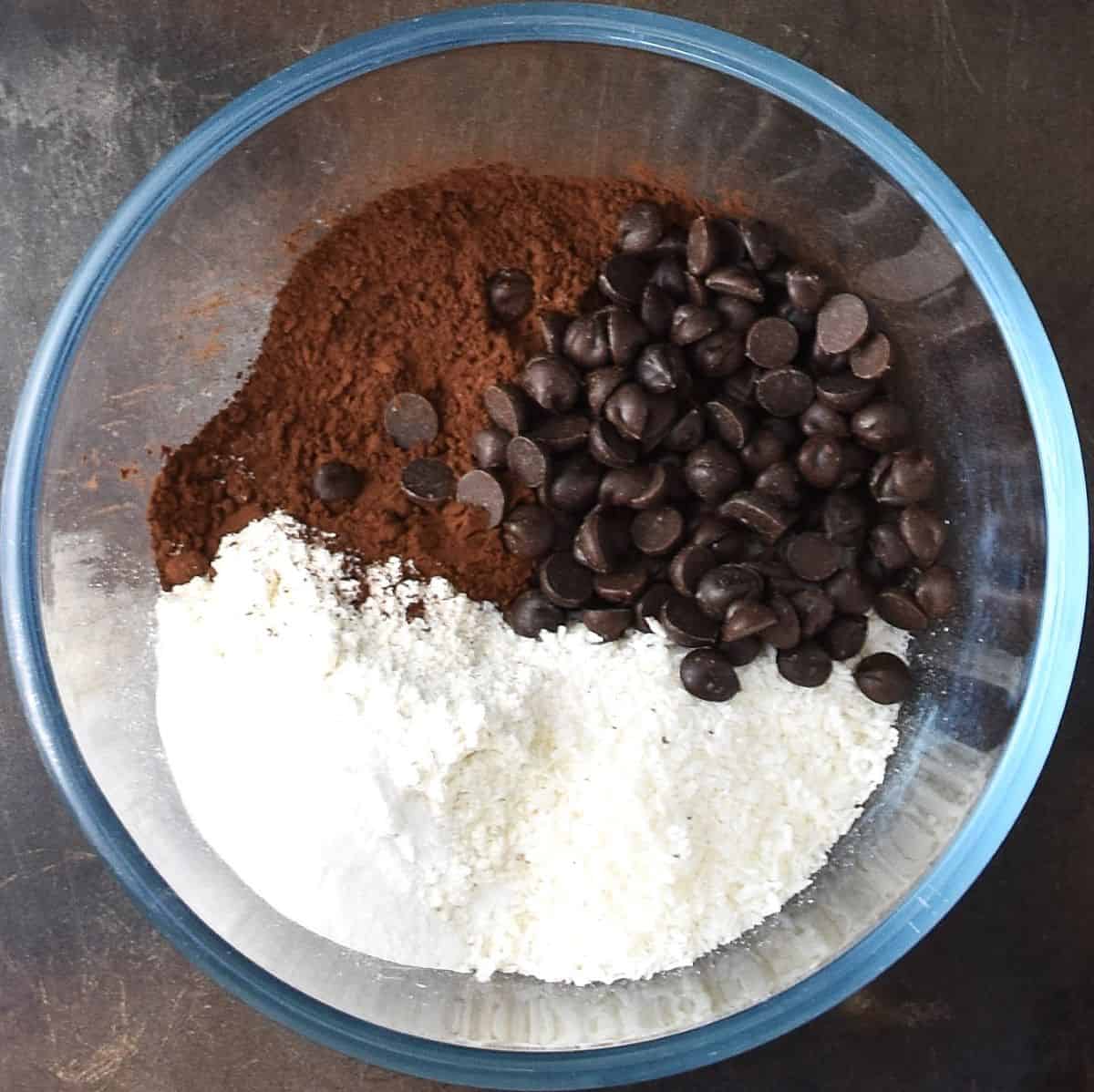Top down view of dry ingredients for chocolate coconut muffins in glass bowl.
