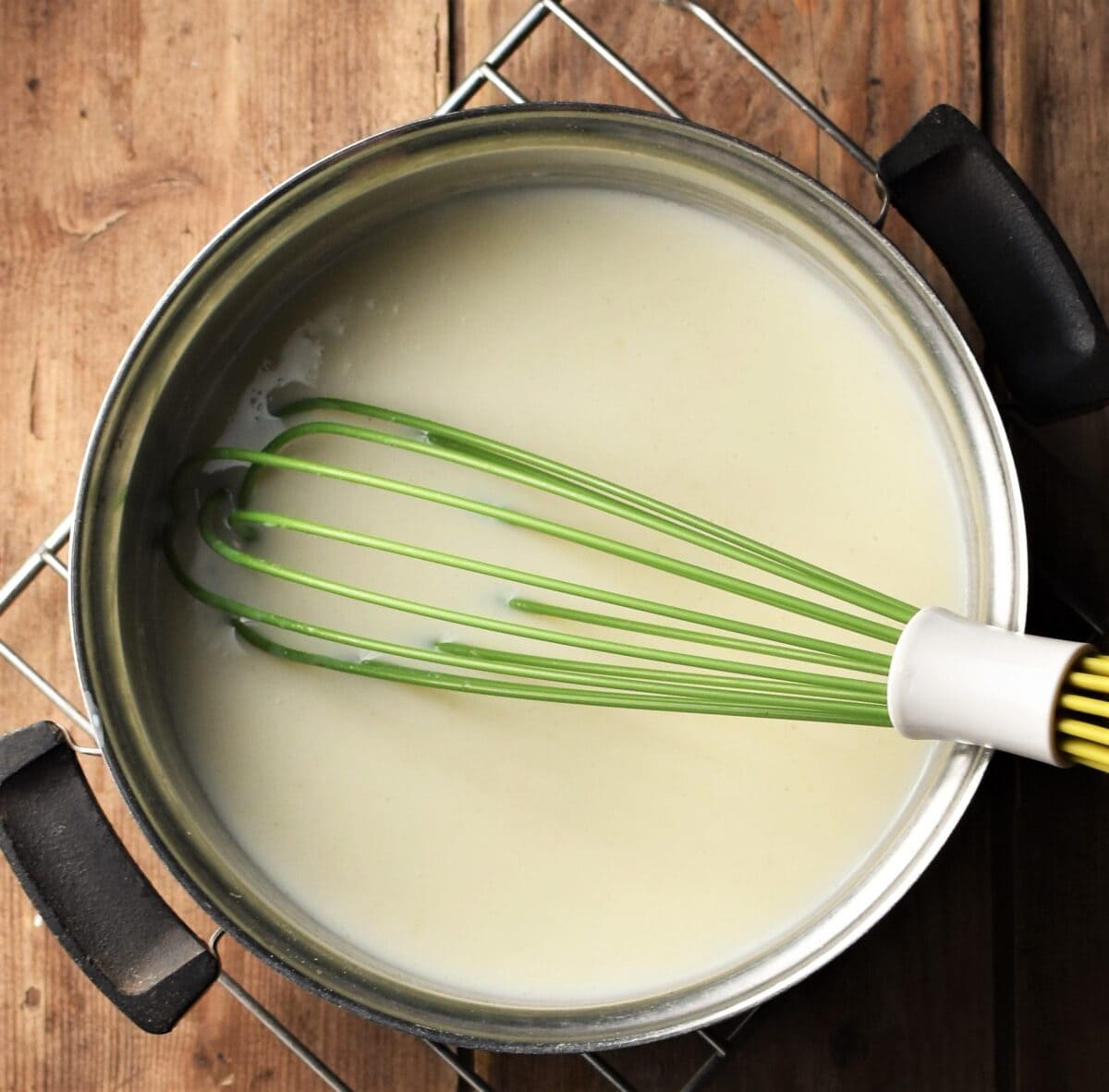 Bechamel sauce in saucepan with green whisk.