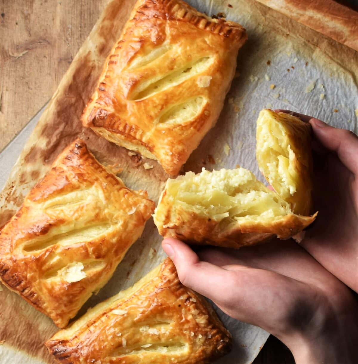 3 cheese and onion pasties on top of paper and 1 held open.