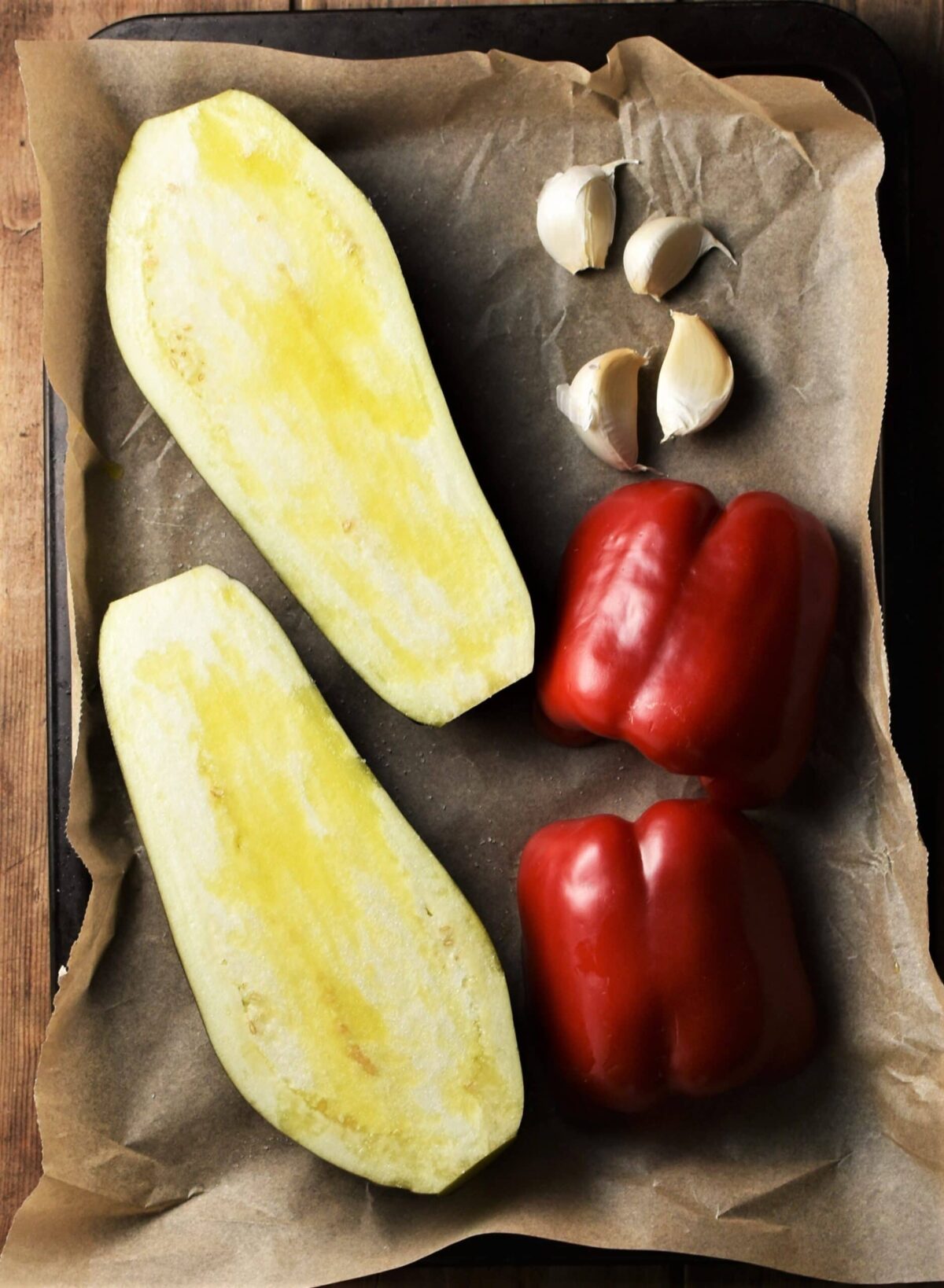 Halved eggplant, red pepper and 4 garlic cloves on top of parchment.