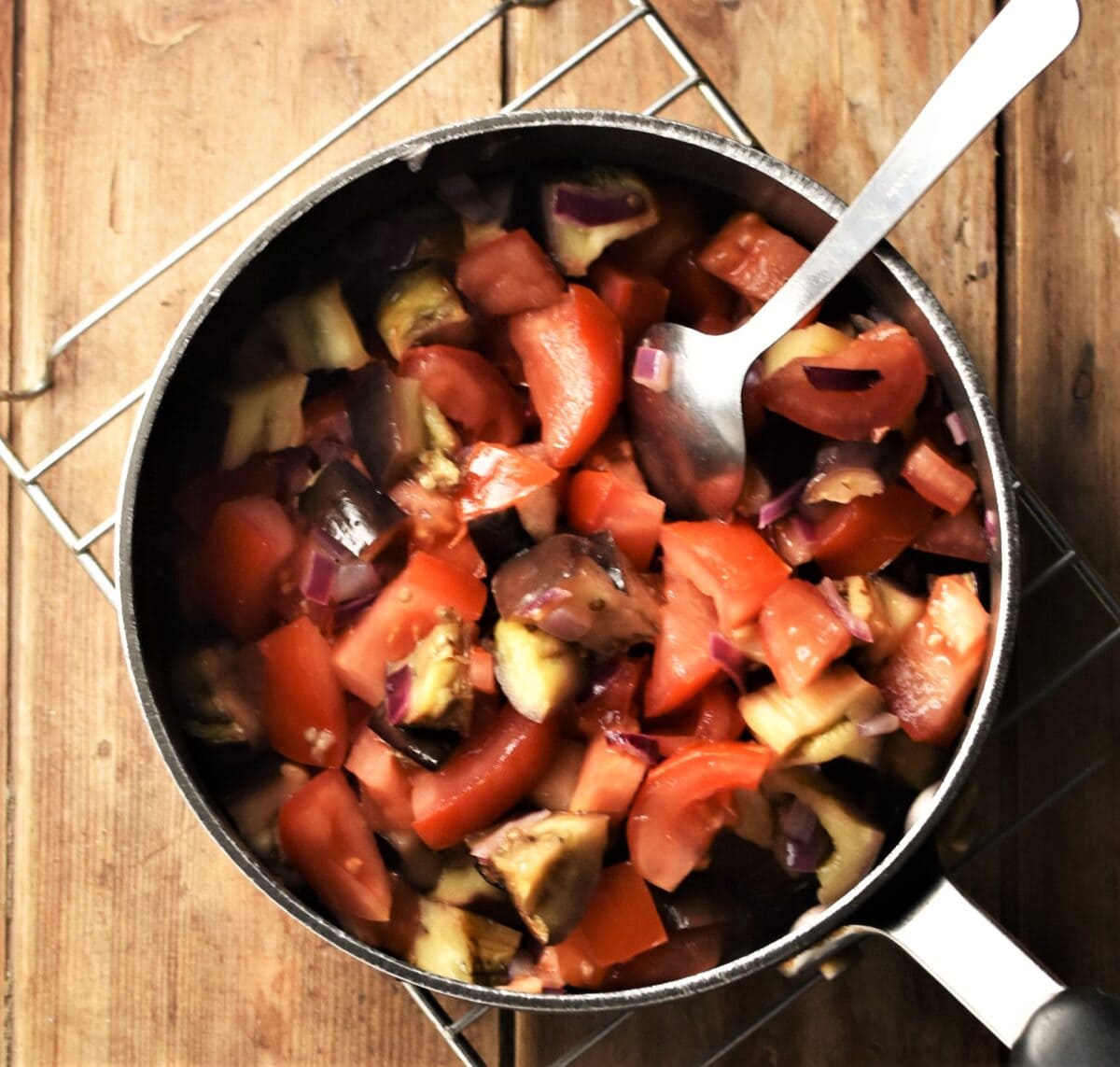 Chopped eggplant and tomato in pot with spoon.