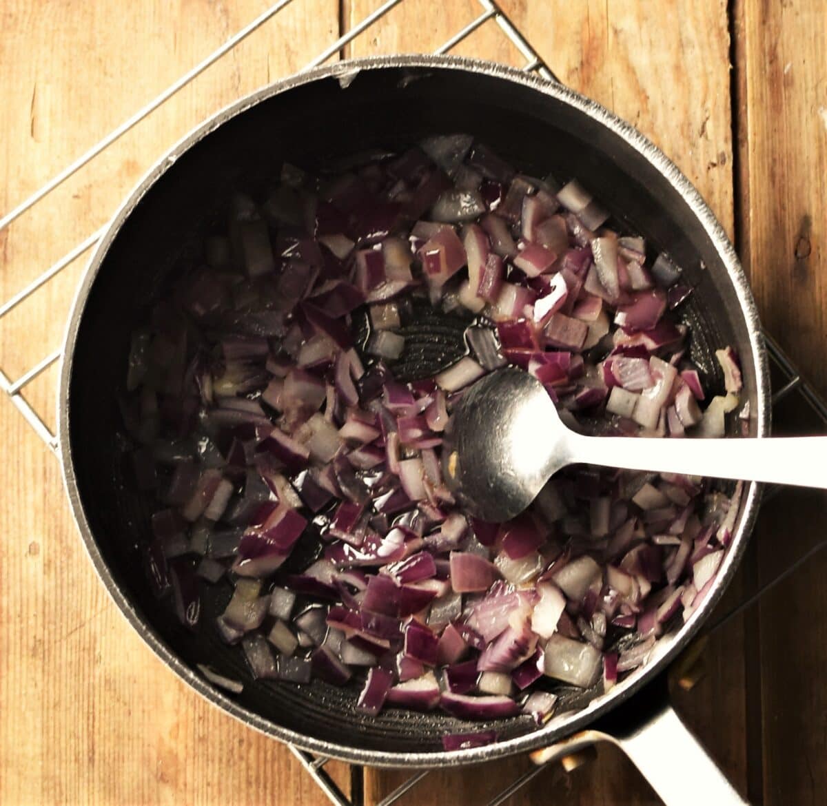 Chopped red onion in large pot with spoon.