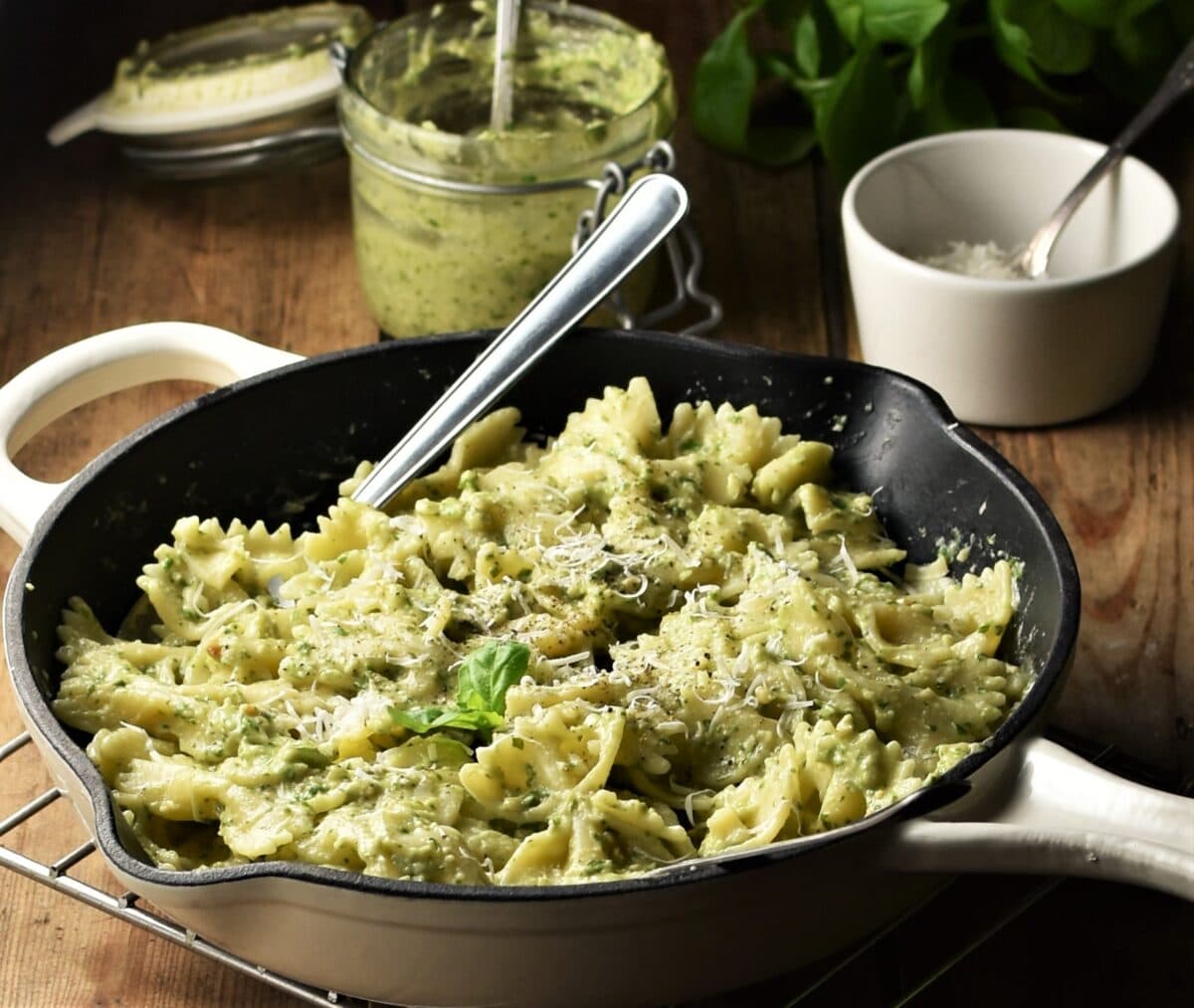 Side view of pasta with pesto in skillet, with pesto in jar in background.