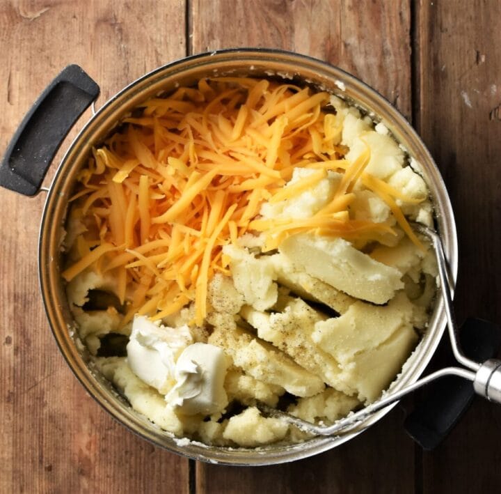 Mashed potato, grated cheese and potato masher in pot.