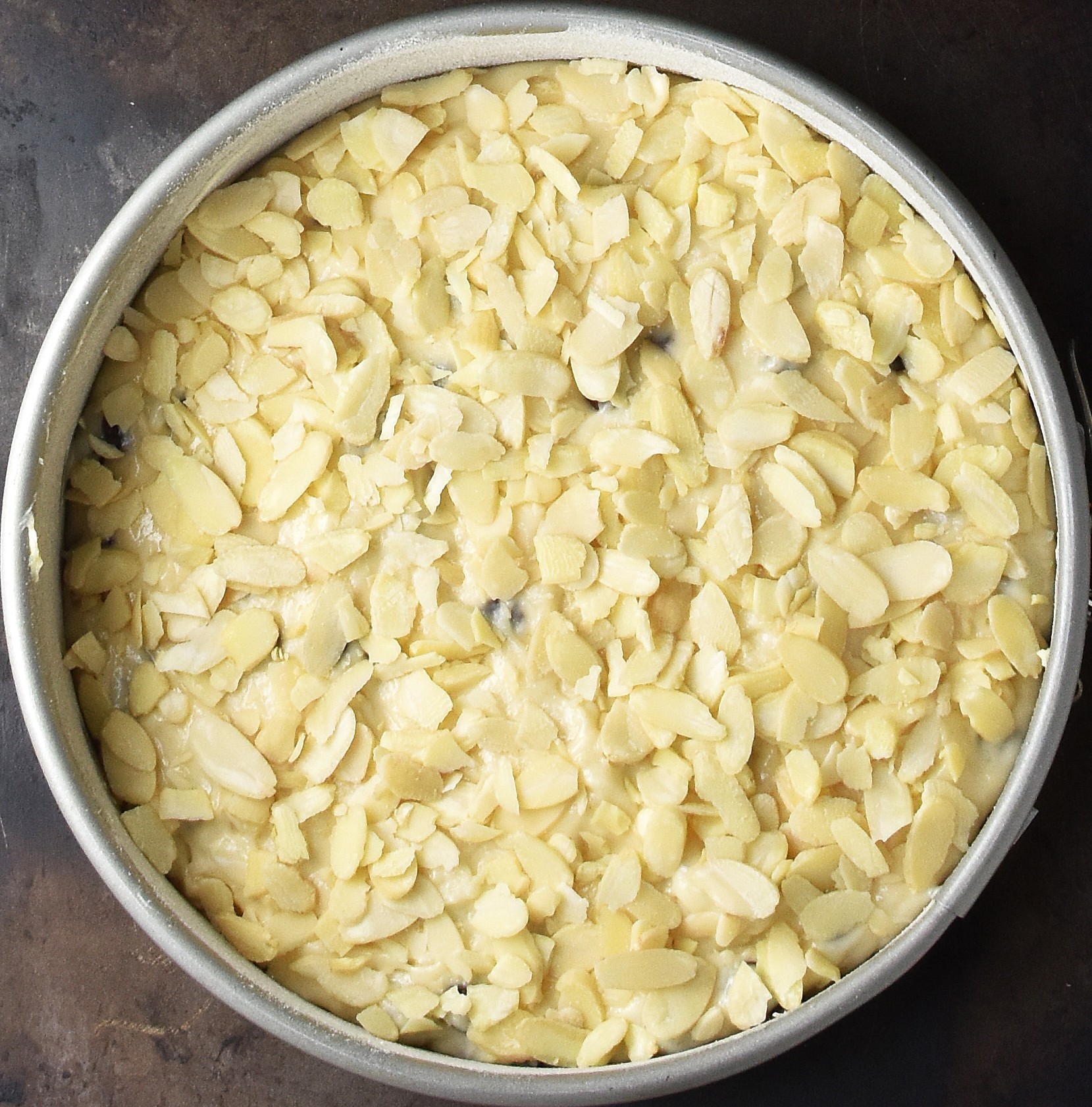 Marzipan cake batter topped with flaked almonds in tin.