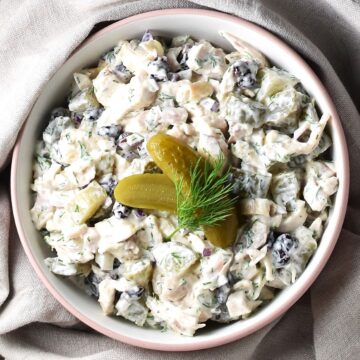 Top down view of chicken salad with dill pickles in white bowl with beige cloth in background.