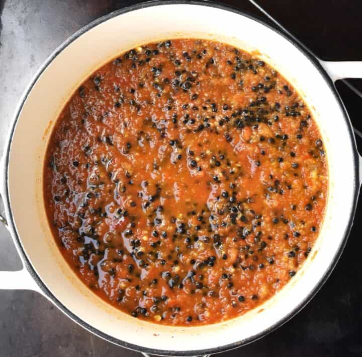 Top down view of black lentils in curry sauce in white pot.
