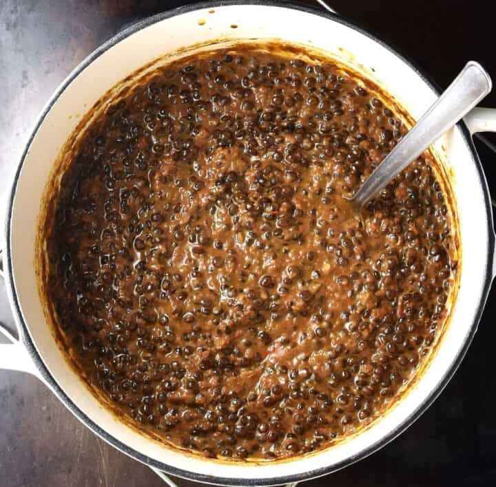 Thick black curry lentil curry in white pot with spoon.