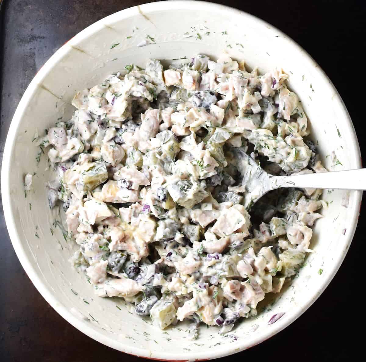 Top down view of creamy dill pickle and chicken salad in white bowl with spoon.