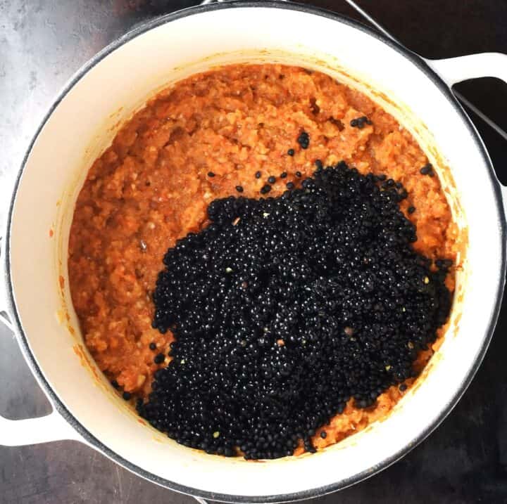 Adding black lentils to vegetables for curry in white pot.