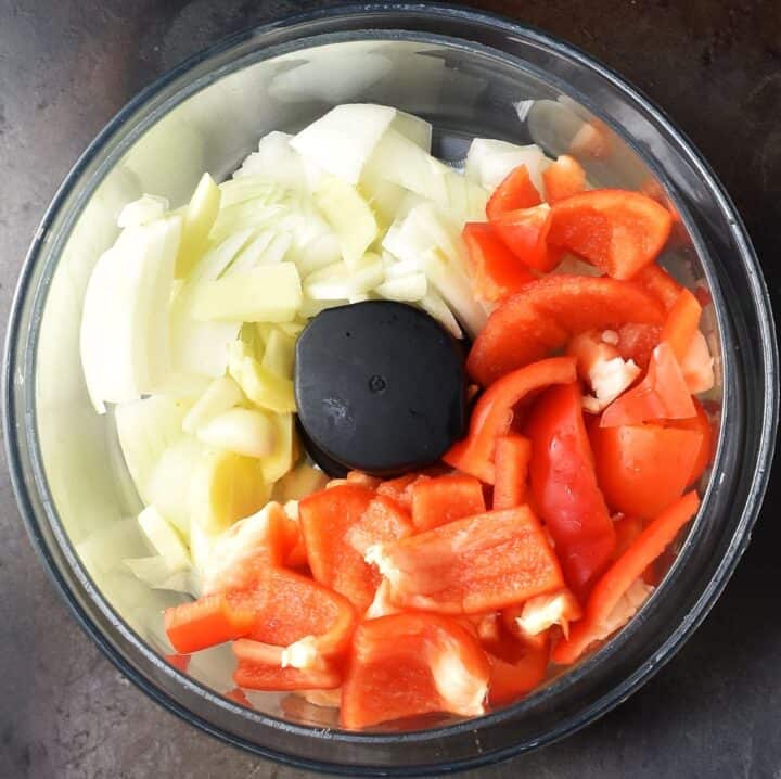 Top down view of onion and pepper in blender bowl.