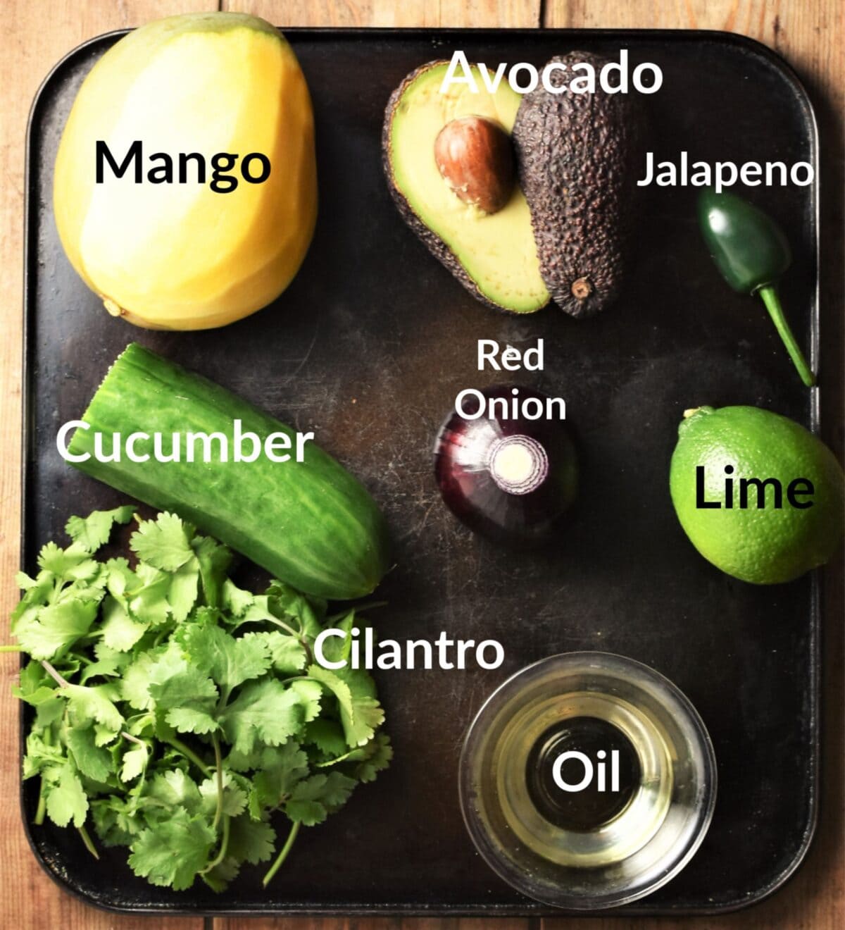 Avocado mango cucumber salsa ingredients on top of dark tray.