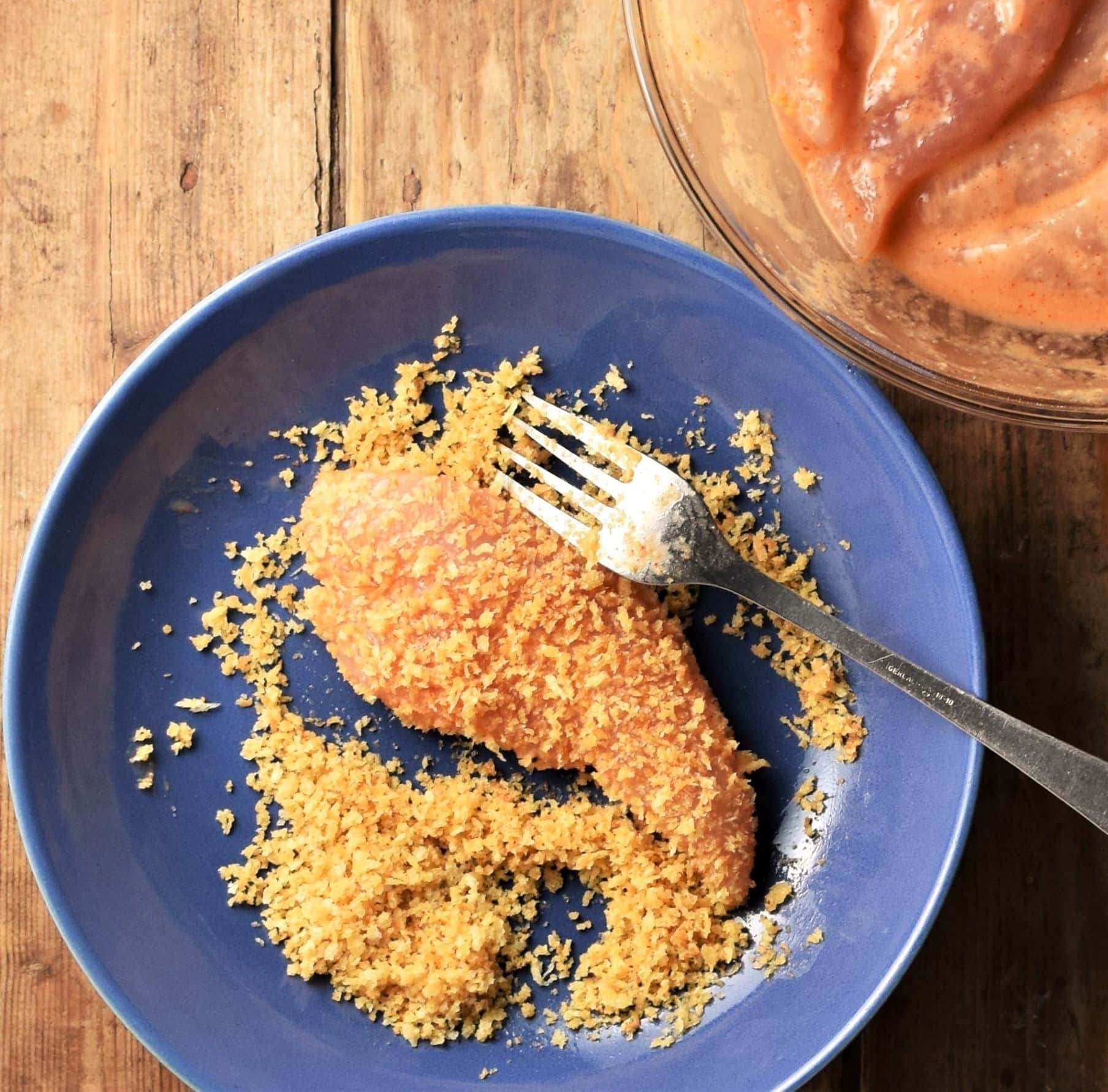 Breaded chicken finger in blue bowl with fork.