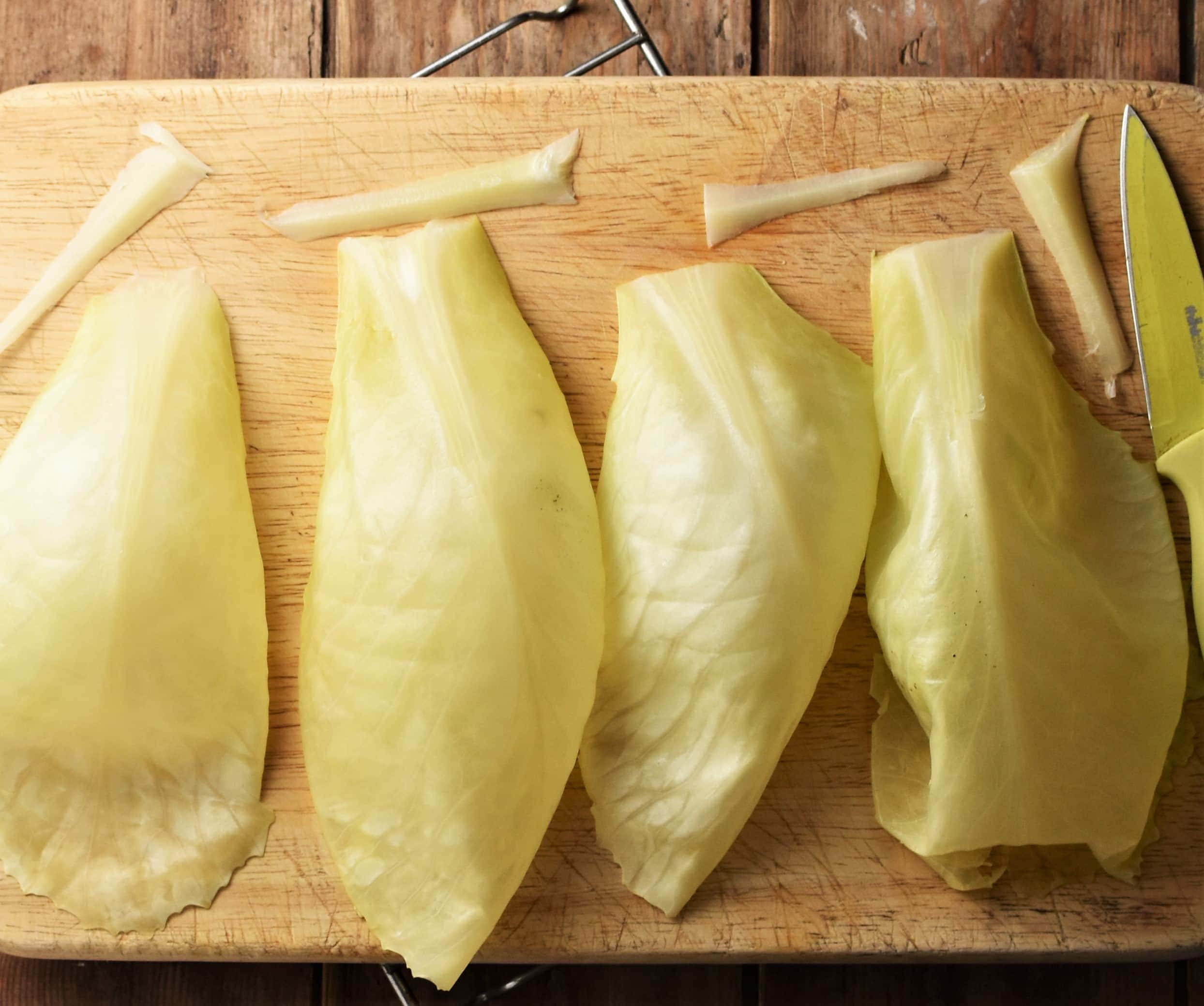 4 cabbage leaves on top of wooden bard with knife.