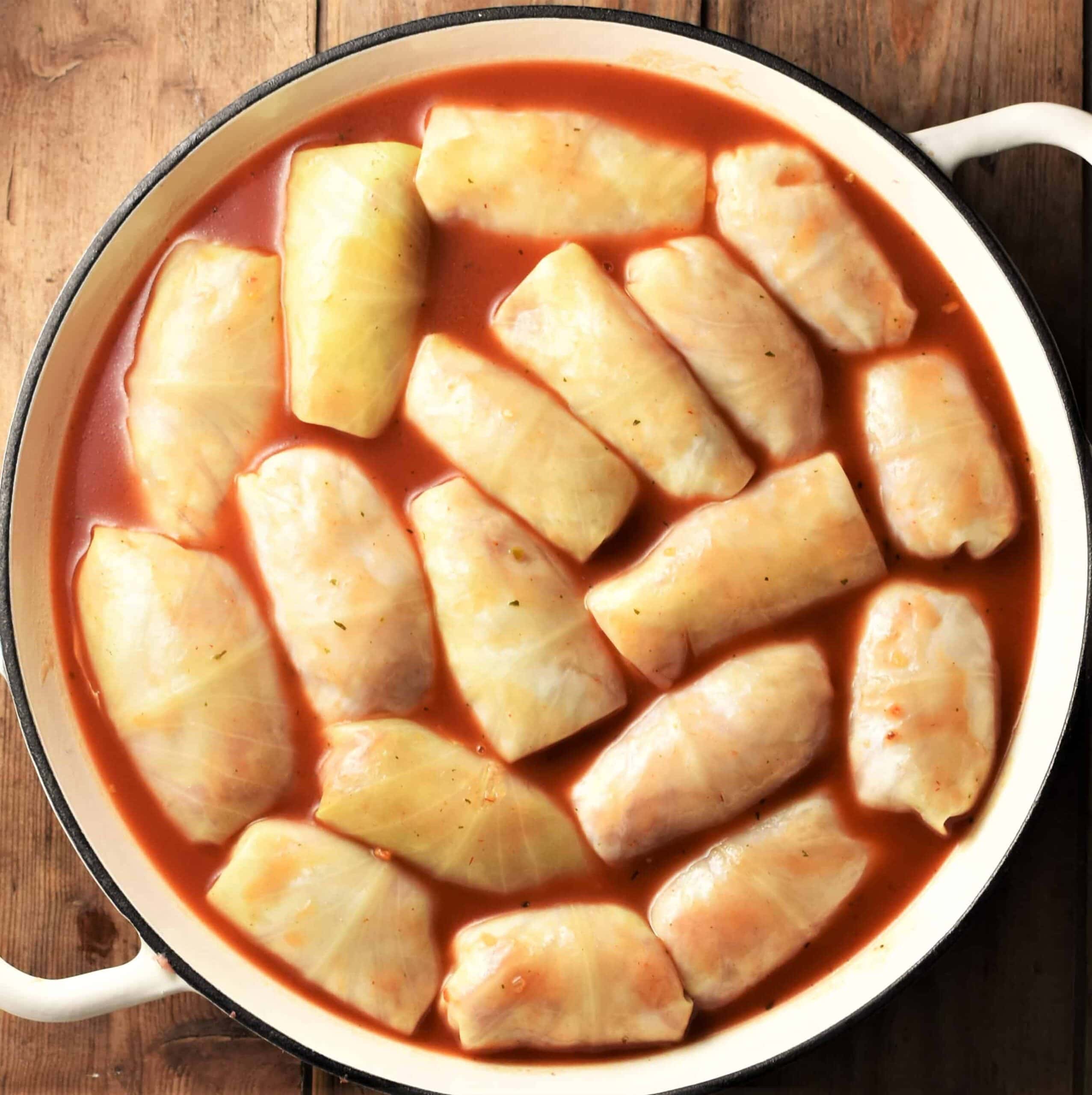 Cabbage rolls in tomato sauce inside large shallow yellow pan.