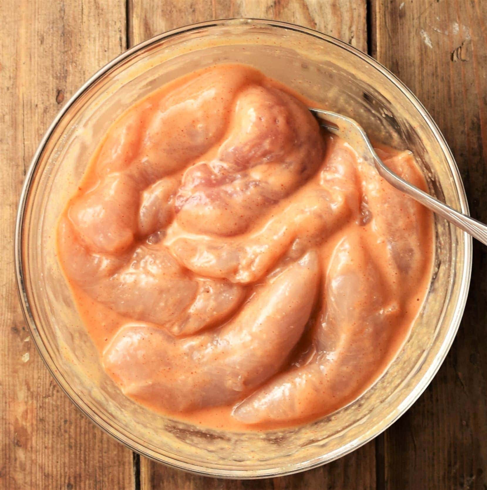 Chicken tenderloins in egg mixture in mixing bowl with fork.