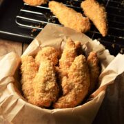 Side view of crispy chicken fingers in bowl lined with parchment.