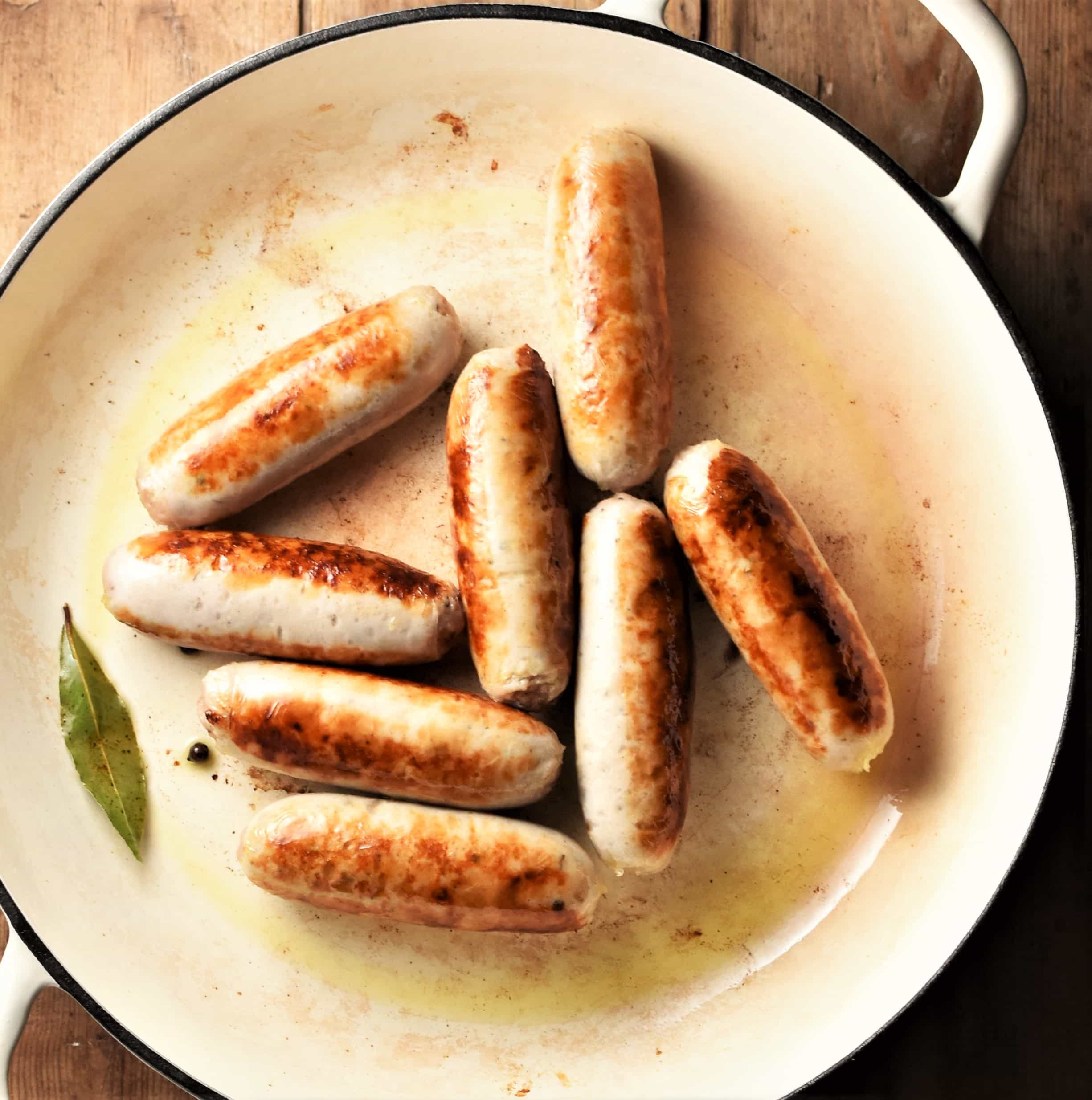 8 fried sausages in large white pan.