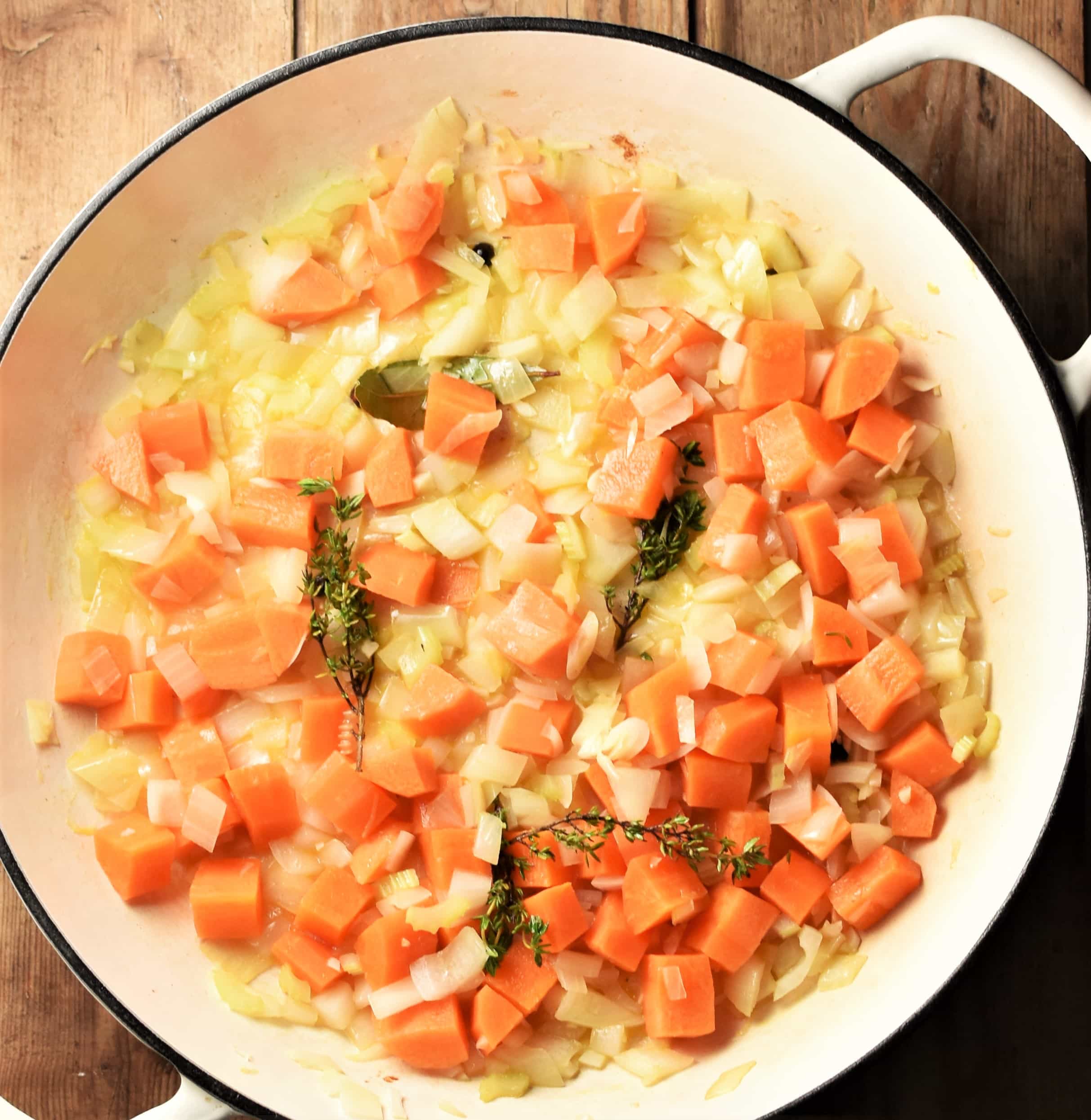 Cubed carrots, chopped onions and herbs in large white pan.