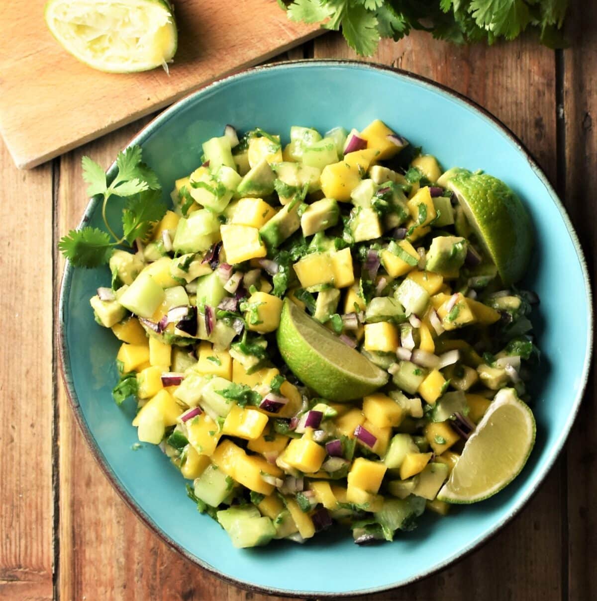 Chunky mango avocado salsa with lime wedges in blue bowl.