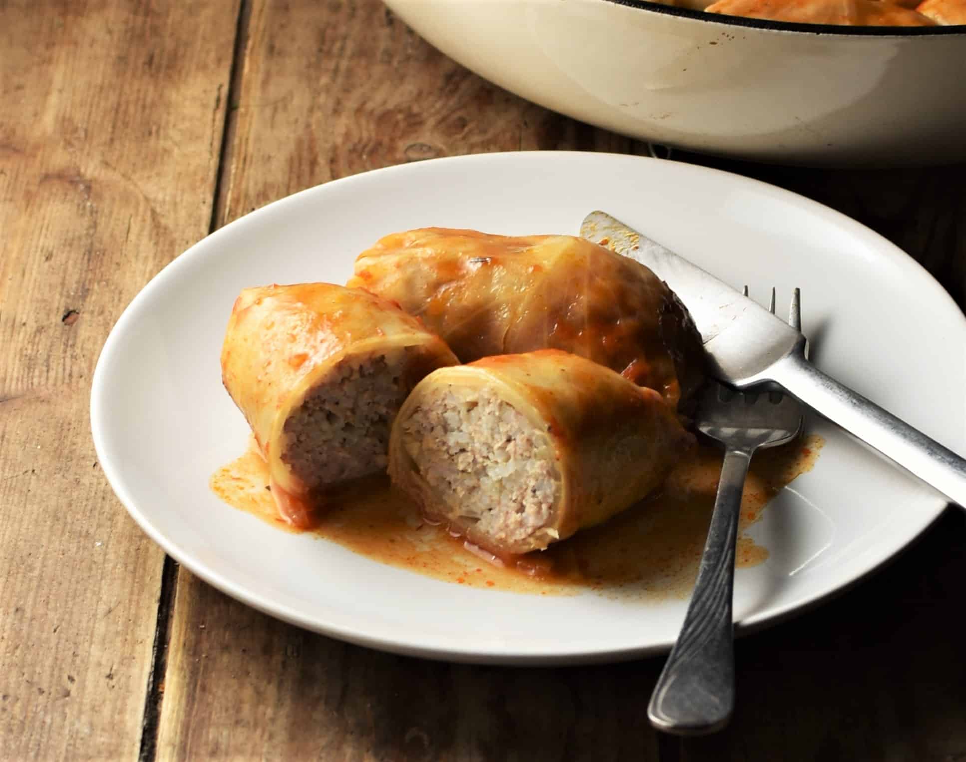 Side view of stuffed cabbage roll cut in half on top of white plate with knife and fork.