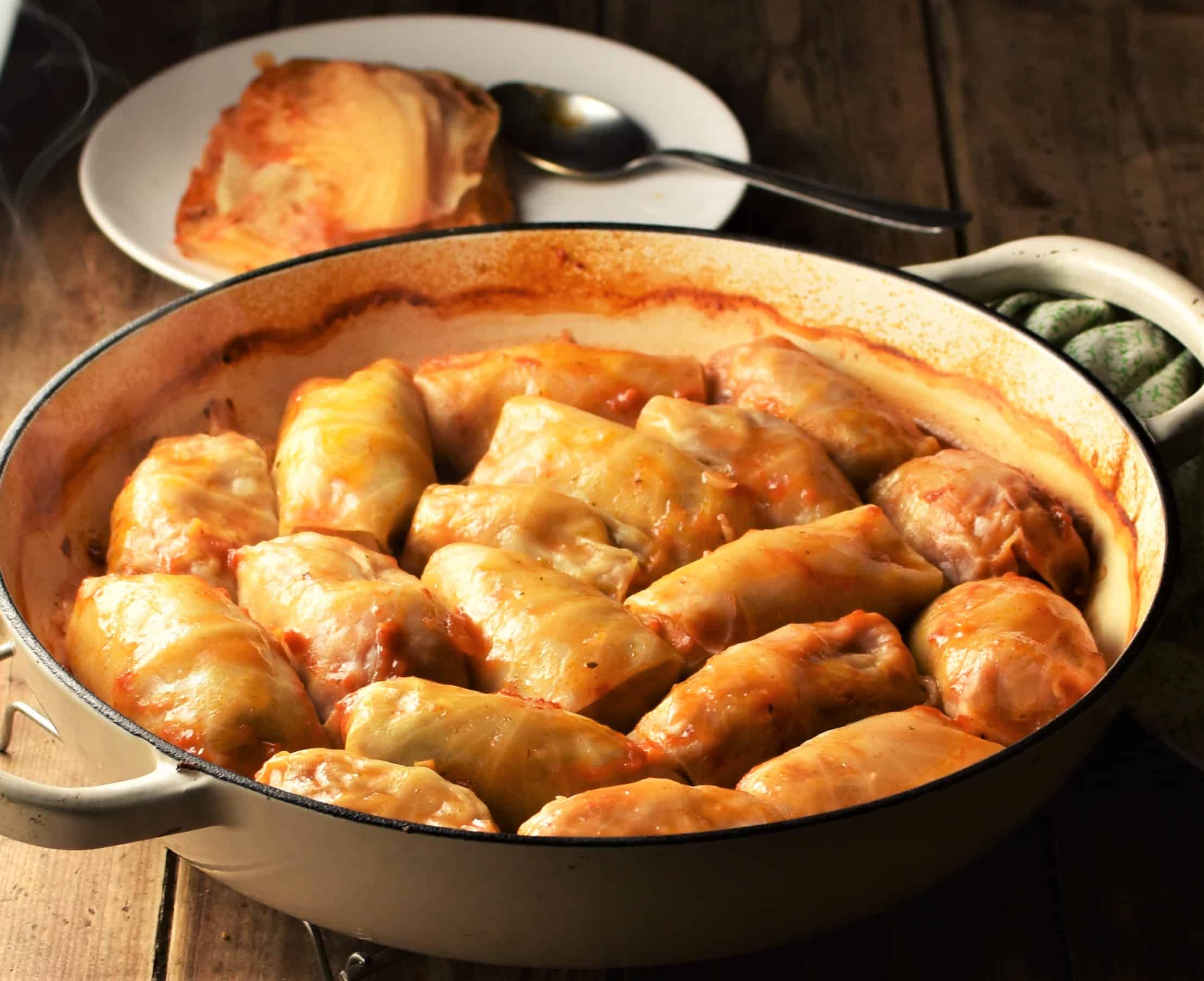 Side view of cabbage rolls in shallow white pan.