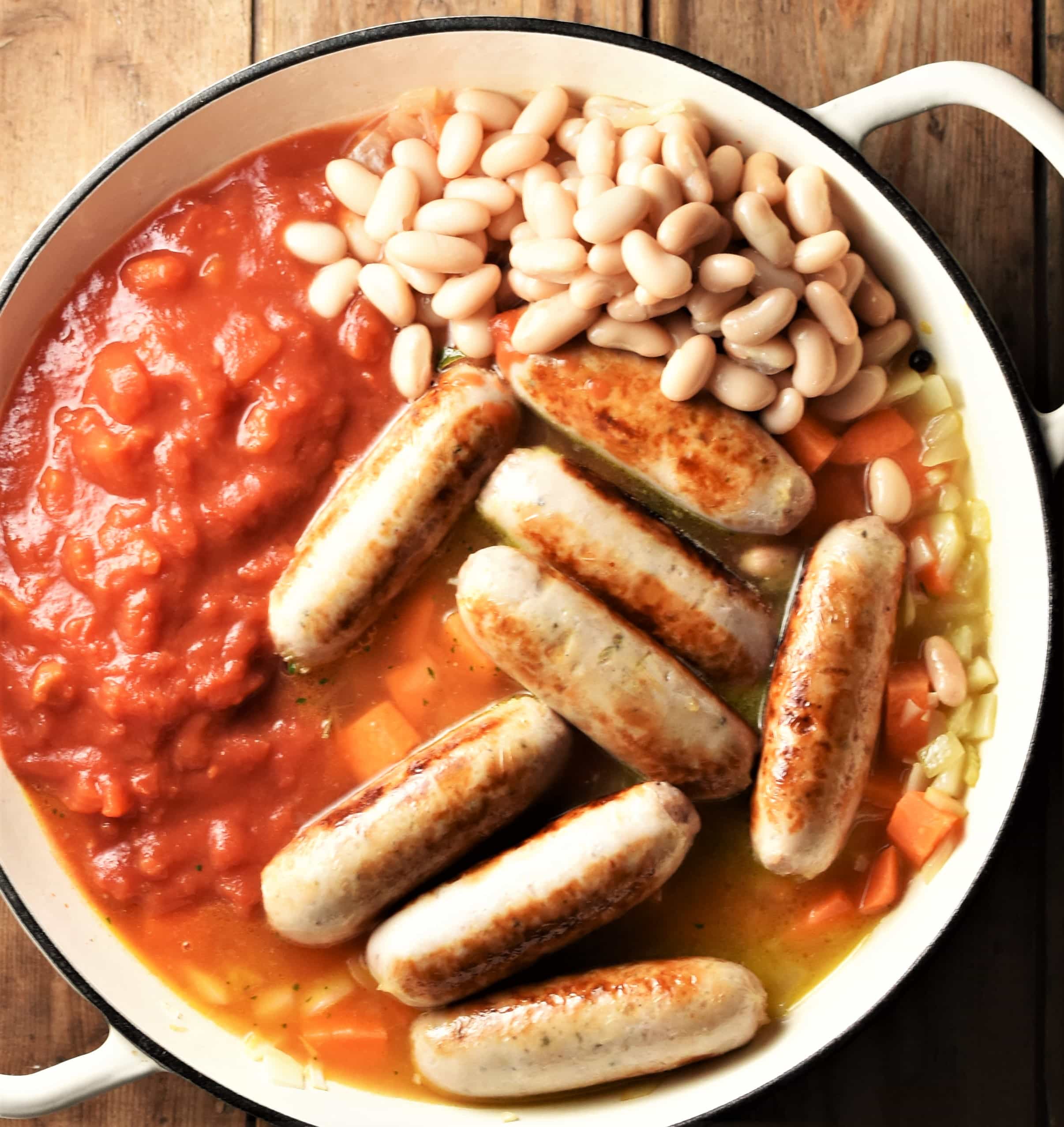 Sausages, chopped tomatoes and beans in white pan.